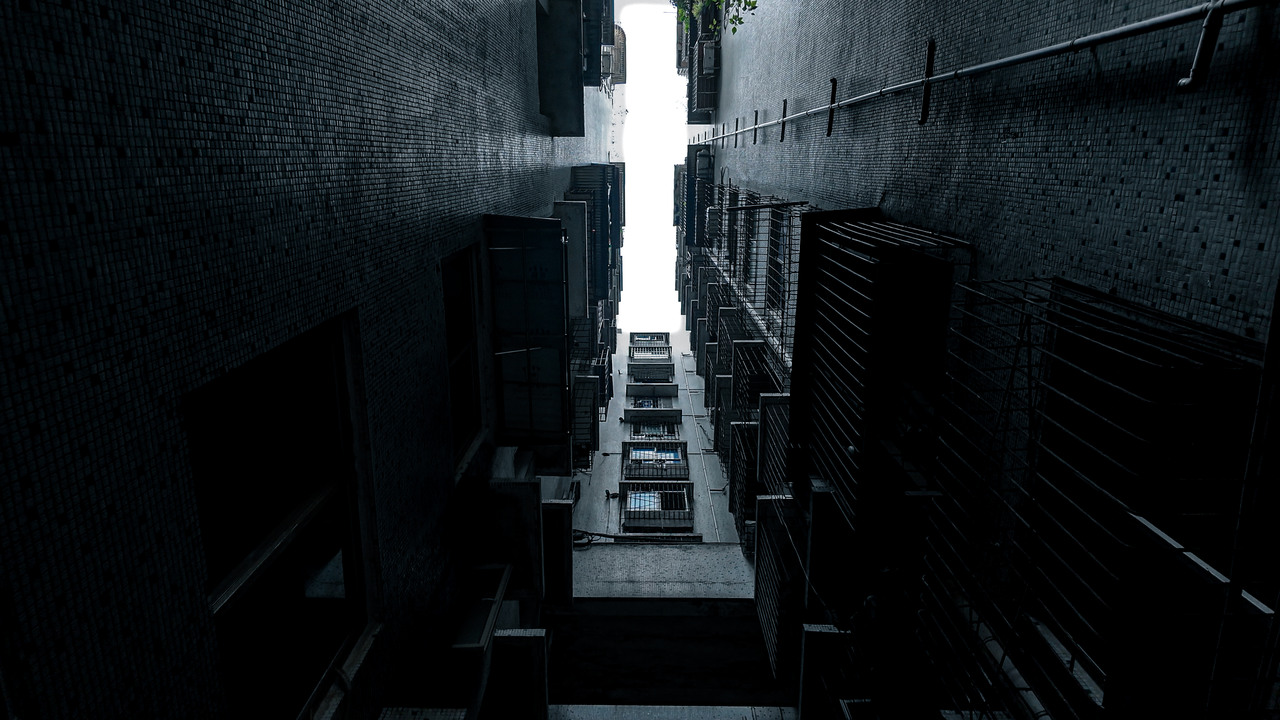 A narrow opening of sky between two dark residential buildings viewed from below.